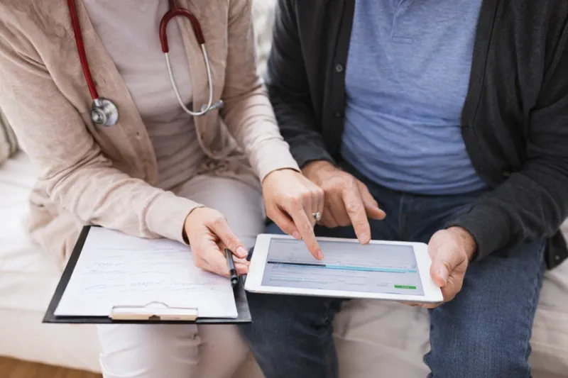 Pflegeperson berät älteren Herrn am Tablet - Beratungssituation Hauskrankenpflege